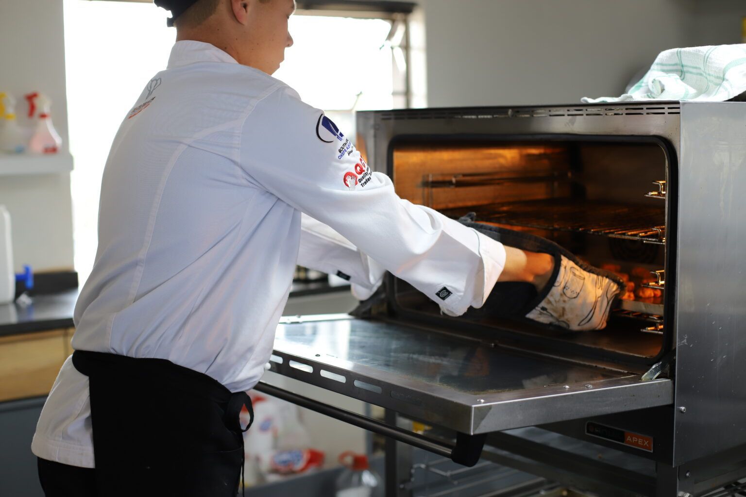 a man in a chef 's uniform is taking something out of an oven
